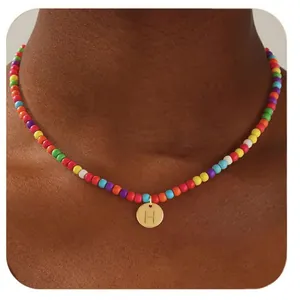 Détail du collier de perles arc-en-ciel avec un pendentif doré rond et la lettre H gravée