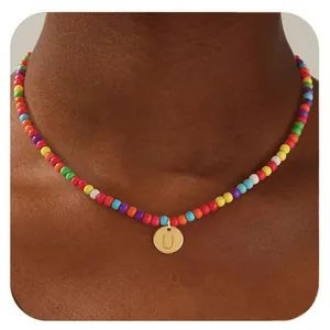 Détail d'un collier de perles colorées avec un pendentif rond doré gravé de la lettre U
