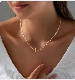 Detail van kralenketting met gouden horizontale kruishanger en ingezette micro-diamanten