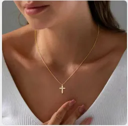 Detail van een minimalistische gouden kruis ketting met fonkelende zirkonia op een model