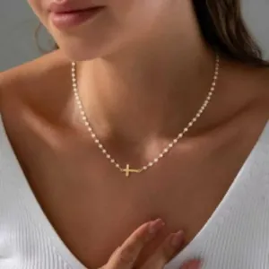 Minimalistische vergulde messing kruisketting met witte kralen gedragen op een modelnek