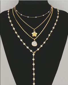 Detail of layered gold-plated necklaces with flower, shell pendants and faux pearls