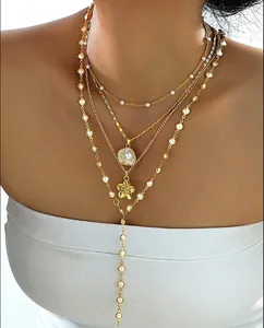 Detail of layered gold-plated necklaces with pearl beads and floral shell pendant