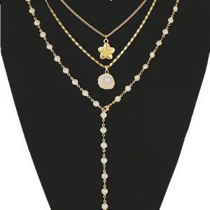 Three-layer gold necklace with flower, shell pendants and white pearls on a black display