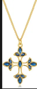 Détail macro du pendentif croix plaqué or avec pierres bleues et accents de fleurs de lys