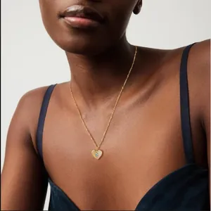 Collier pendentif coeur doré avec pierre bleue et diamants sur le cou d'un modèle