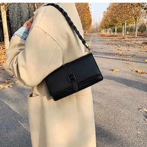 Détail d'un sac bandoulière en cuir noir avec bandoulière tressée sur un manteau beige