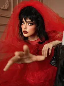 Détail d'une robe gothique rouge en tulle avec perruque noire bouclée et voile assorti
