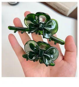 Macro detail of two dark green acetate bow hair clips held in hand for scale