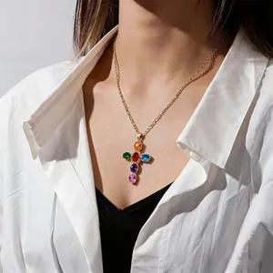 Détail d'un collier chaîne dorée avec un pendentif croix orné de pierres colorées