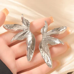 Silver leaf earrings with hammered metal texture held in hand against satin background