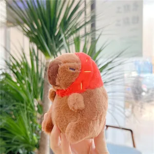Close-up of a plush capybara wearing a red cap being held in a hand outdoors