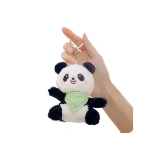 Plush panda keychain with green polka dot bib held in hand for scale on white background