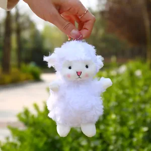 Cute white plush sheep charm with pink embroidery details held in a sunny park setting