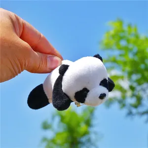 Cute plush panda brooch held against a sunny blue sky background with green trees
