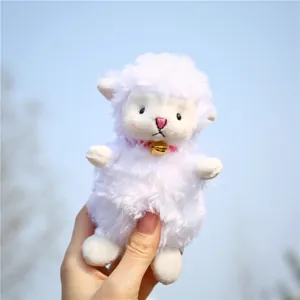Close-up of white plush lamb pendant with pink nose, rosy cheeks and a gold bell