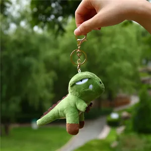 Close-up of a green plush dinosaur keychain with golden metal clasp in nature