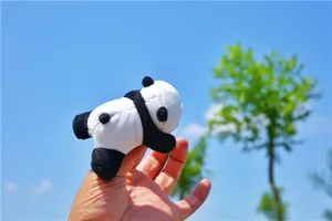 Close-up of a miniature plush panda keychain held by hand against a sunny sky background