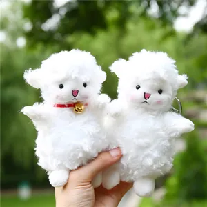 Plush lamb keychain duo with golden bell and soft fur shown in an outdoor setting