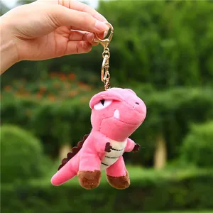 Pink plush dinosaur keychain with golden metal clasp and striped belly on green background