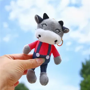 Cute gray and white plush cow keychain in red shirt and denim overalls with sky background
