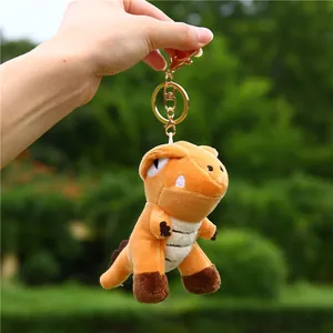 Orange dinosaur plush keychain with golden metal clasp shown in a natural outdoor setting