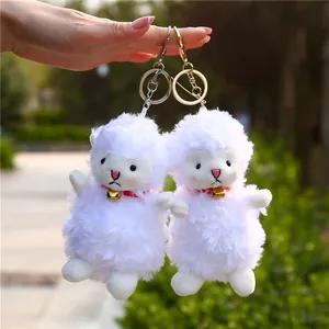 Plush lamb keychains with white faux wool and golden bell charms on a garden background