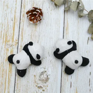 Close-up of two plush panda brooches on a rustic wood background with natural pine cones
