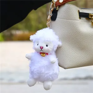 Cute white plush sheep pendant with red collar and bell hanging on a leather bag