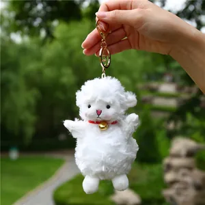 Close-up of white plush sheep keychain with golden bell and metal ring on garden background