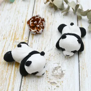 Detailed view of two plush panda brooches on a rustic white wood background with pinecones