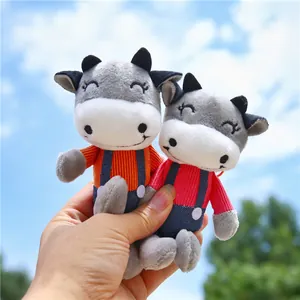Cute plush cow doll keychains in pink and orange outfits with soft grey white fur details