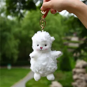 Close-up of white plush lamb keychain with gold metal clasp held in hand outdoors