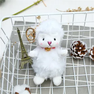 Detail of white plush lamb keychain with golden bell and metal ring in a gift basket