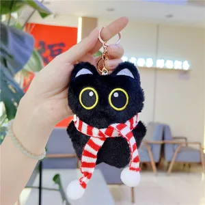 Close-up of black plush cat keychain with yellow eyes and a red striped scarf
