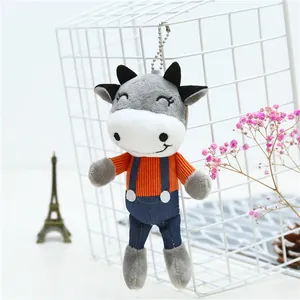 Detail of cute cow plush keychain with striped shirt and denim overalls on a white grid