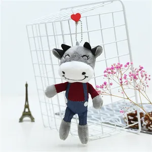 Detail shot of a grey plush cow keychain with embroidered smile on a metal grid