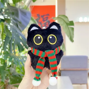 Close-up of black plush cat keychain with red and green striped knit scarf detail