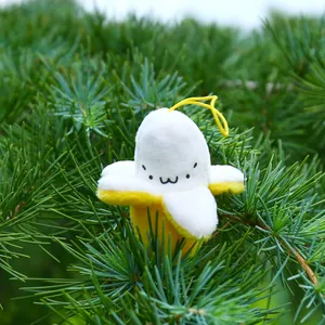 Cute banana plush keychain with a smiling face hanging on a green pine tree branch