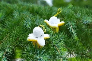 Close-up of cute plush banana charms with facial expressions hanging on green pine branches