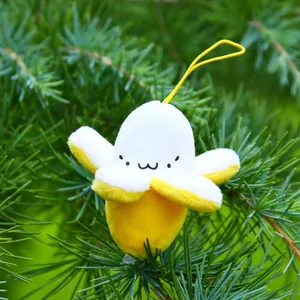 Close-up of cute peeled banana plush keychain with emoji face on natural pine background