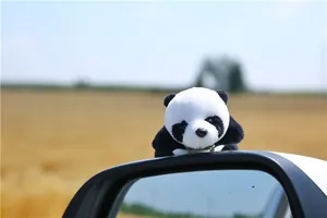 Cute plush panda brooch attached to a car side mirror with a sunny landscape background