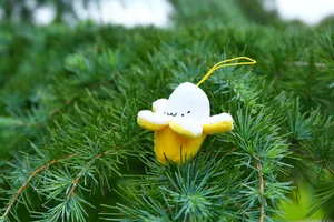 Close-up of cute plush banana charm with smiling face hanging on pine tree branches