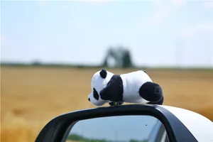 Close-up of a plush panda car ornament mounted on a side mirror with soft furry texture