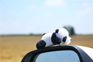 Detailed view of a cute plush panda charm hanging on a car mirror with a scenic background