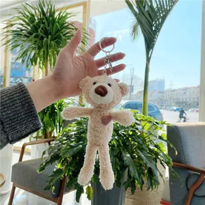 Gros plan d'un porte-clés ours en peluche beige avec cœur rose tenu à la main sur un sac