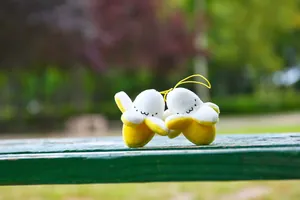 Close-up of two cute plush banana pendants with peel-off design on green bench