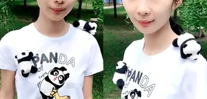 Detail showing cute plush panda brooch accessory pinned on a white t-shirt shoulder