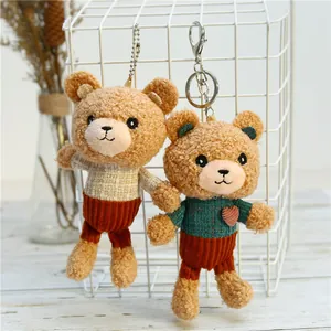 Detail of two plush teddy bear keychains in knitted outfits on a white grid display