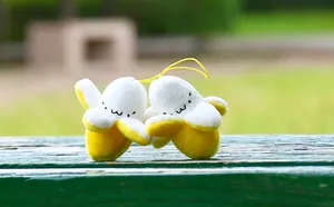 Close-up of two cute plush banana charms with facial expressions on a park bench